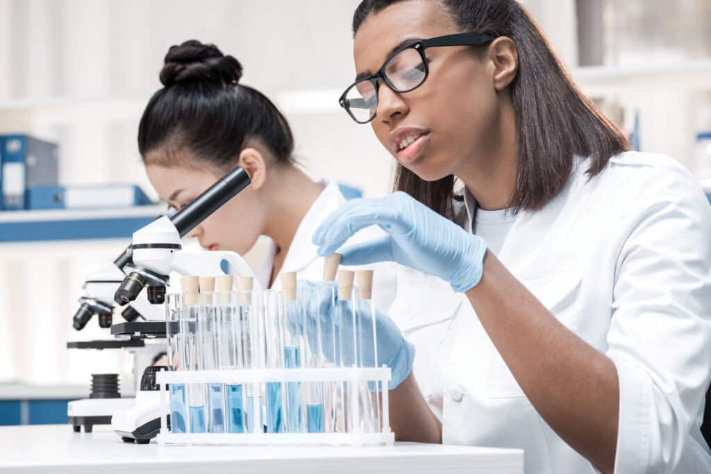 Professional young scientists working with microscope and test tubes in chemical laboratory